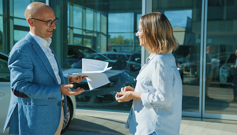 Conseiller remettant des documents à une cliente devant un véhicule.
