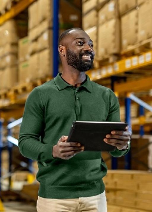Homme souriant au milieu d'un entrepôt avec un carnet à la main