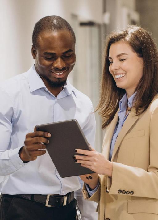 Deux personnes souriantes regardent ensemble une tablette. Elles semblent collaborer ou discuter dans un environnement professionnel.