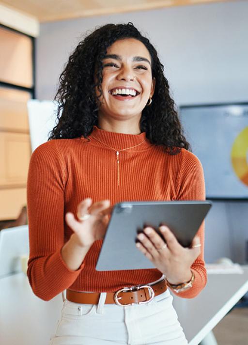 Une femme souriante tient une tablette dans un espace de travail lumineux, probablement un bureau moderne.