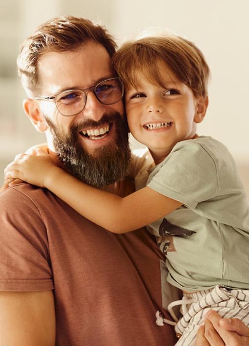 Père avec son enfant dans les bras, tous deux sourient.