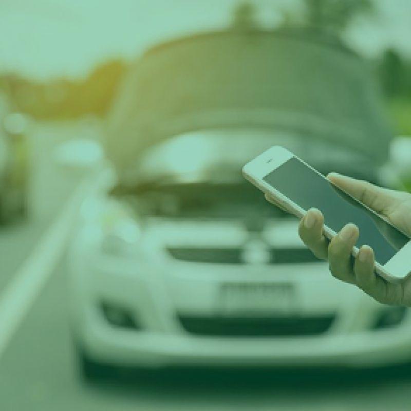 Une personne appelle une assistance devant une voiture au capot ouvert