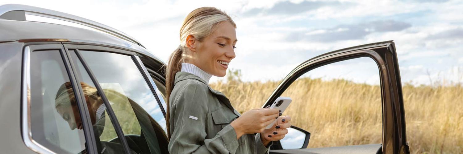 Femme adossée à une voiture regardant son téléphone