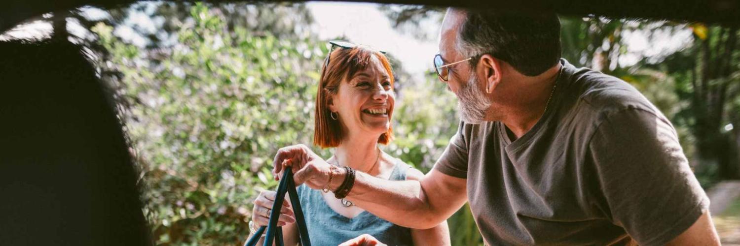 Un homme et une femme sourient en rangeant des affaires dans le coffre d’une voiture