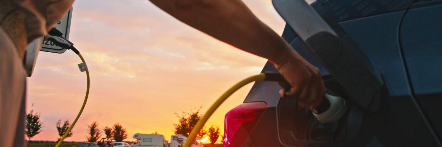 Une personne recharge sa voiture sur un couché de soleil