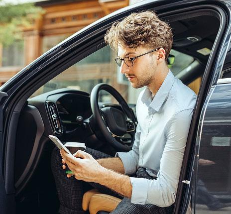 Un homme assis au volant d’une voiture porte ouverte sur ton téléphone